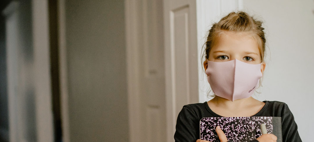 Niña pequeña con una mascarilla puesta en la cara y sujetando un cuaderno