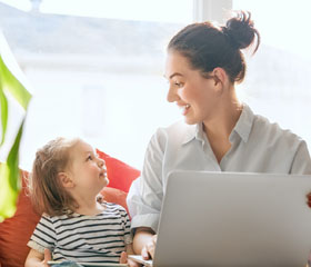 Mujer sosteniendo un ordenador y sonriendo a su hija que está al lado de ella con una tablet